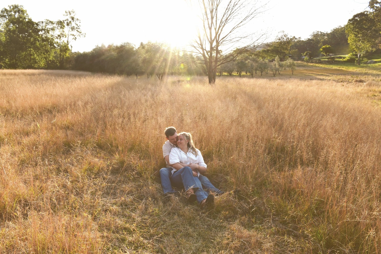 Couple seated in golden grass with hills behind them